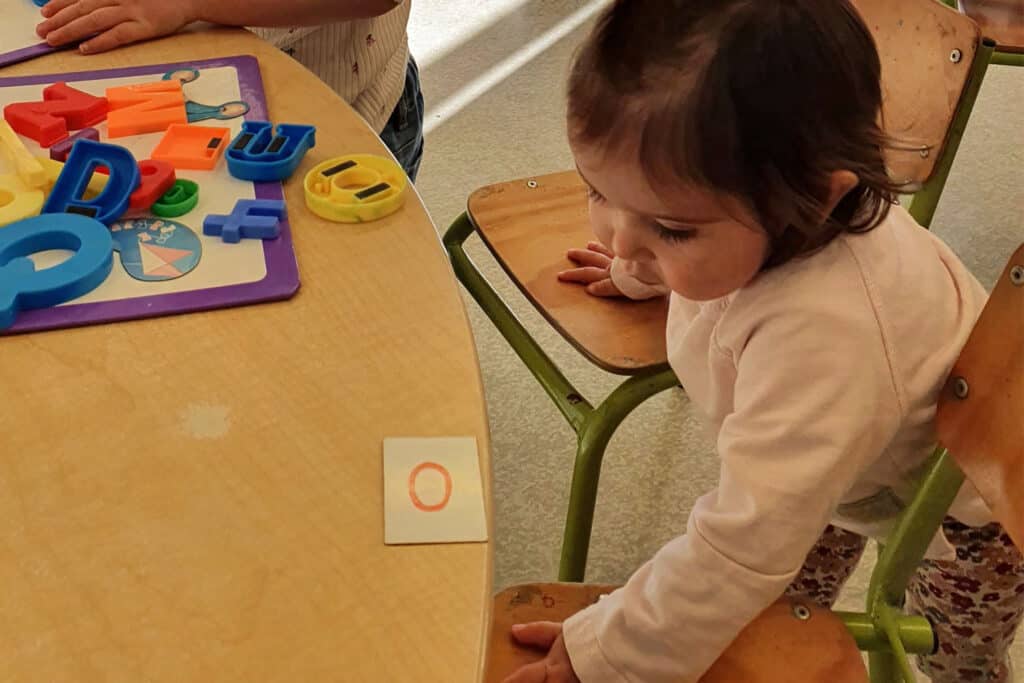 One-year-old finds chairs at kindergarten table are high and hard to get onto.