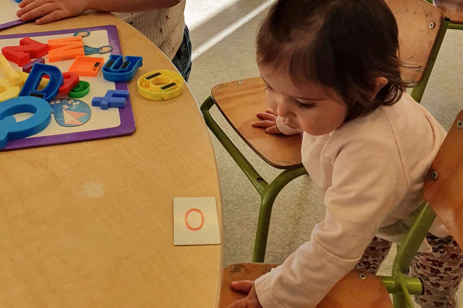 One-year-old finds chairs at kindergarten table are high and hard to get onto.