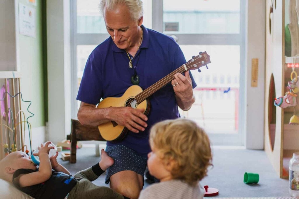 NZ teacher playing ukulele to infants scene - attentive quality care
