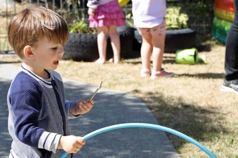Boy has found a stick and considers what to do next in his kindy play.