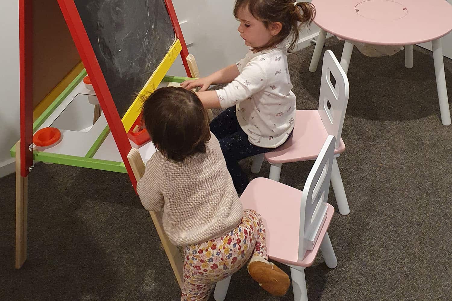Toddler and pre-schooler children sitting at kindy chalk board.