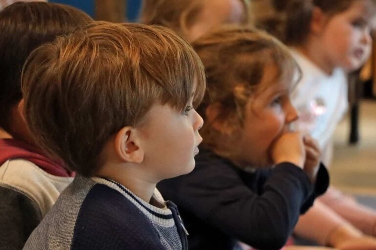Children listening attentively to teacher at early childhood centre mat-time image of the Office of Early Childhood Education (OECE).