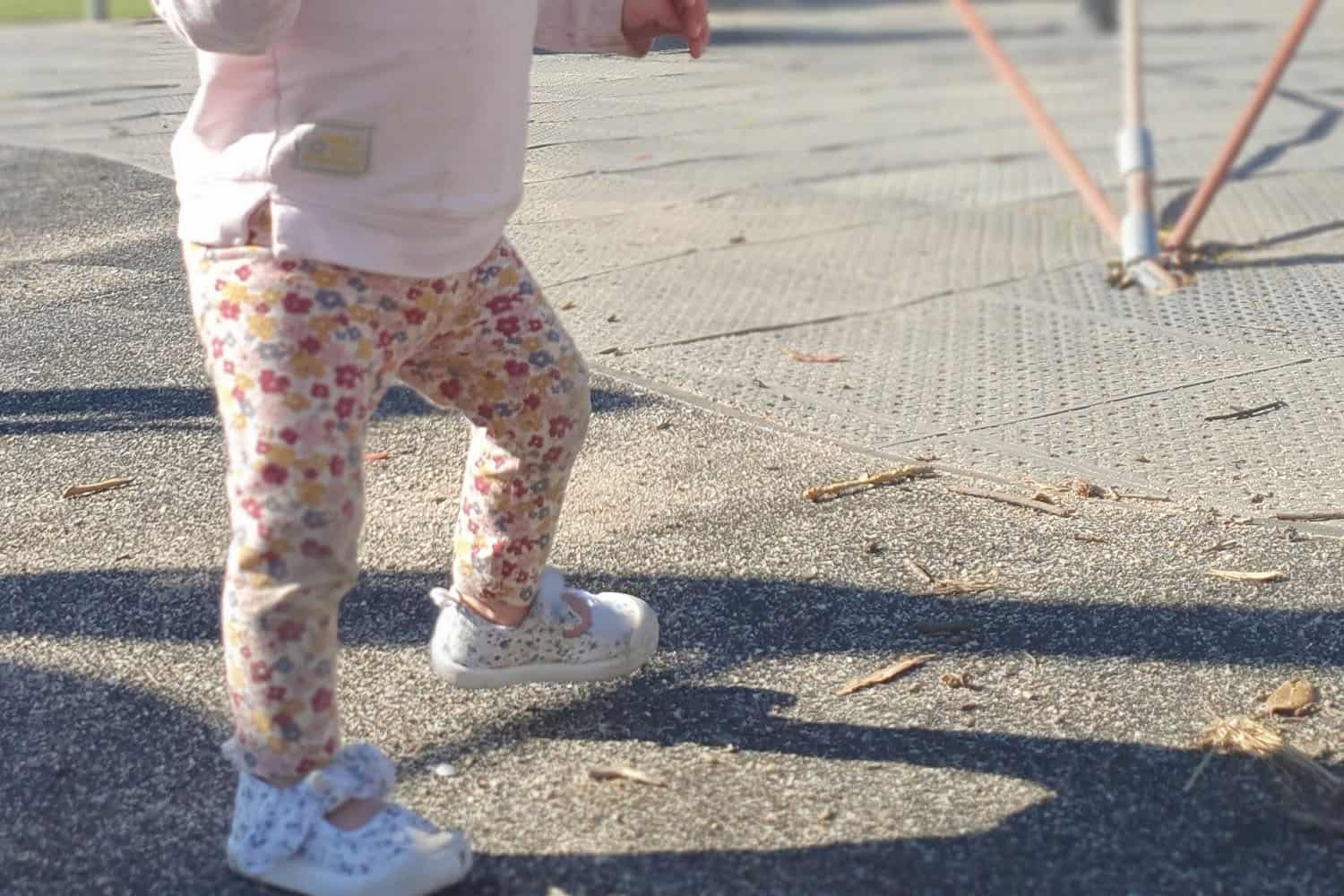 toddler walking on concrete and over to safety surface at playground.
