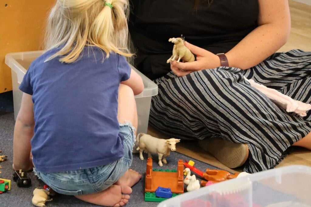 Child and teacher playing with toy farm animal block set.
