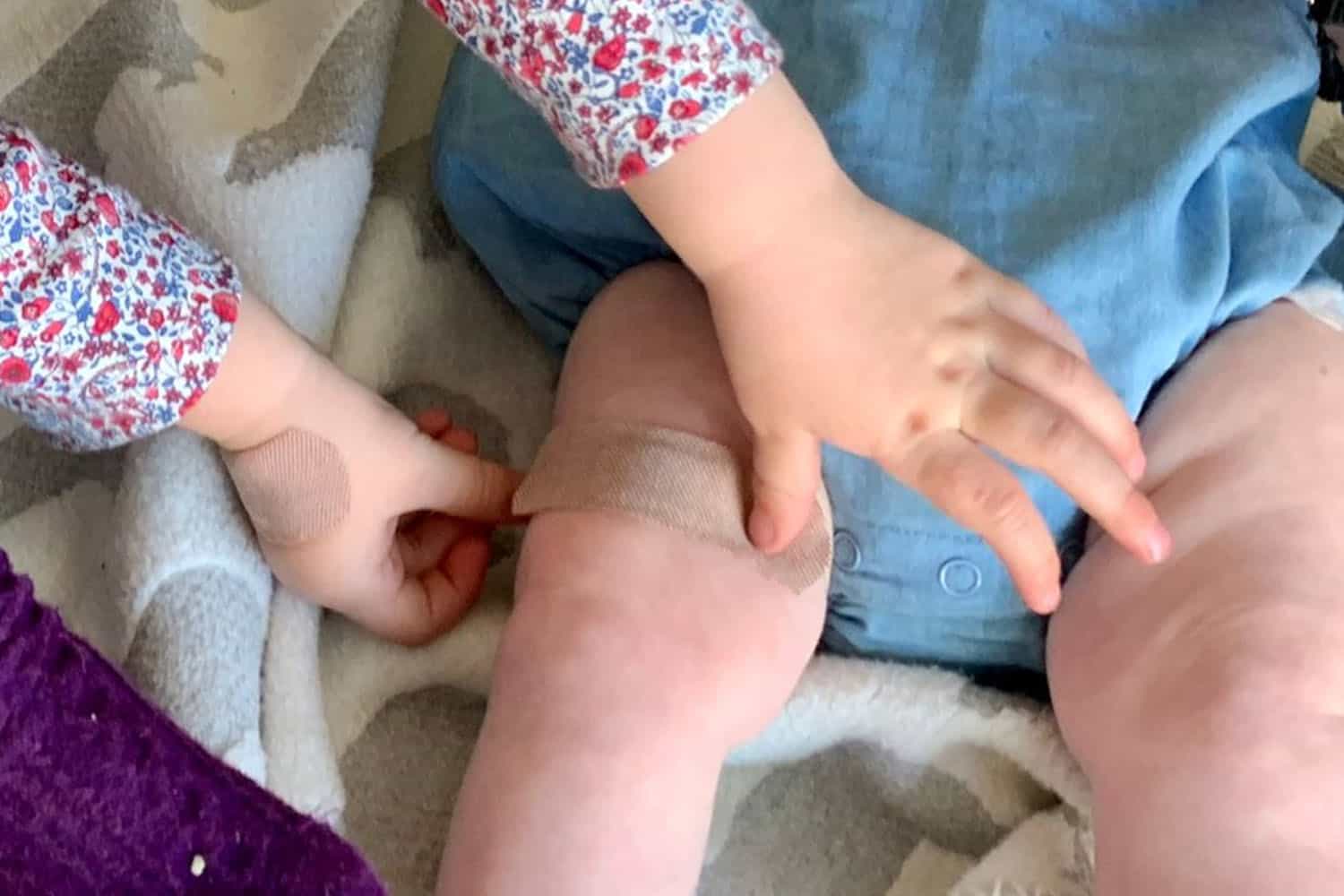 Child playing nurses and doctors, puts a plaster on an a baby's leg.