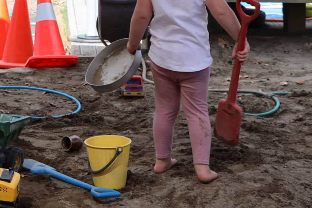 sandpit play child with spade and pan to till with sand
