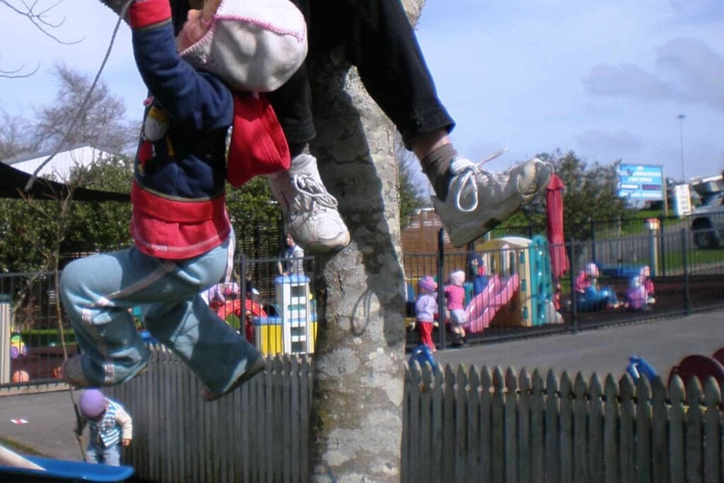 child climbs tree with teacher at early childhood centre