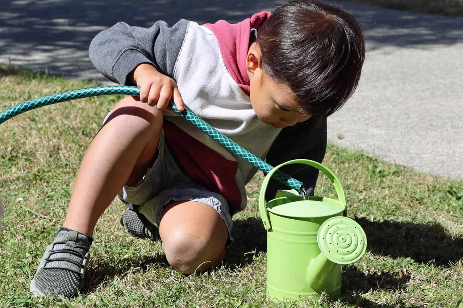 child filling watering can using hose